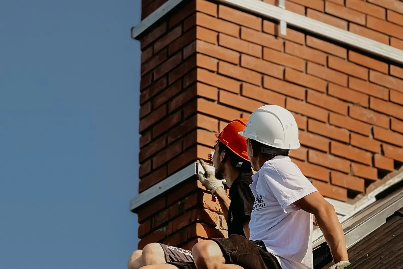 Roofer in a hard hat working beside a brick chimney