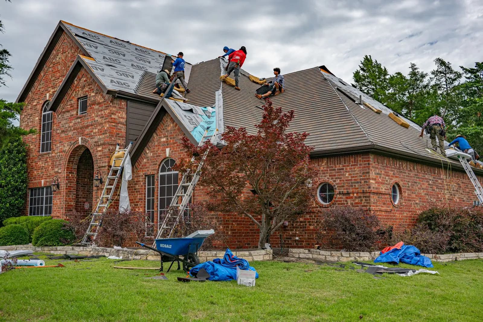 Roofers re-roofing a brick home in Texas with ladders against the eaves